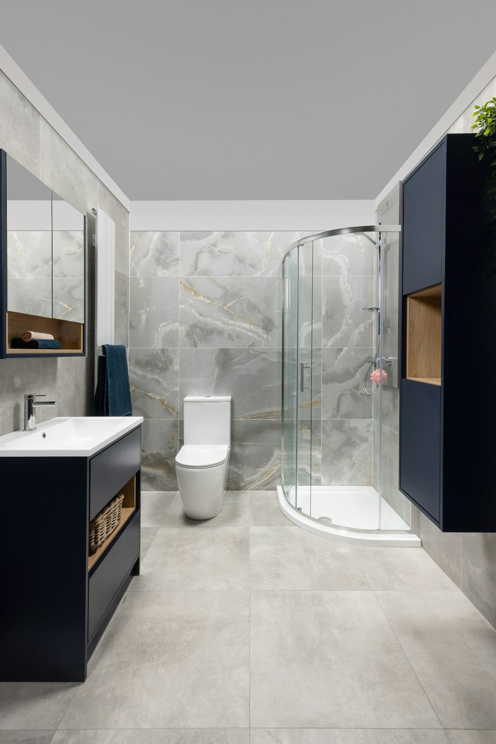 Remodeled bathroom with a navy vanity, marble-look tile and a glass shower