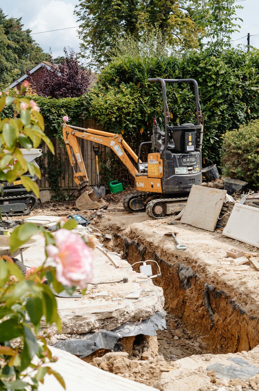 Compact excavator digging a drainage trench in a backyard