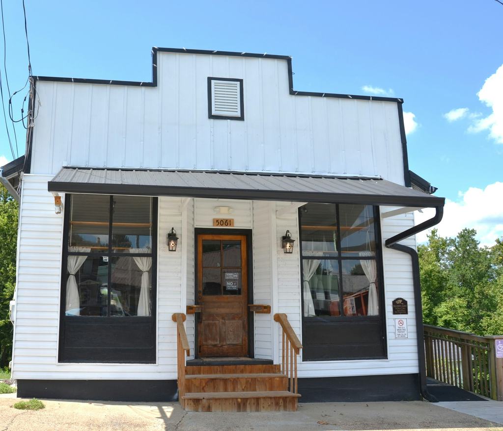Small white storefront building with a wood door and large front windows